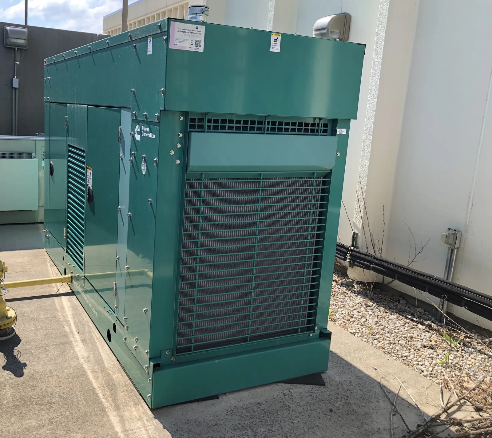 Green Cummins sound-attenuated generator canopy installed beside a building